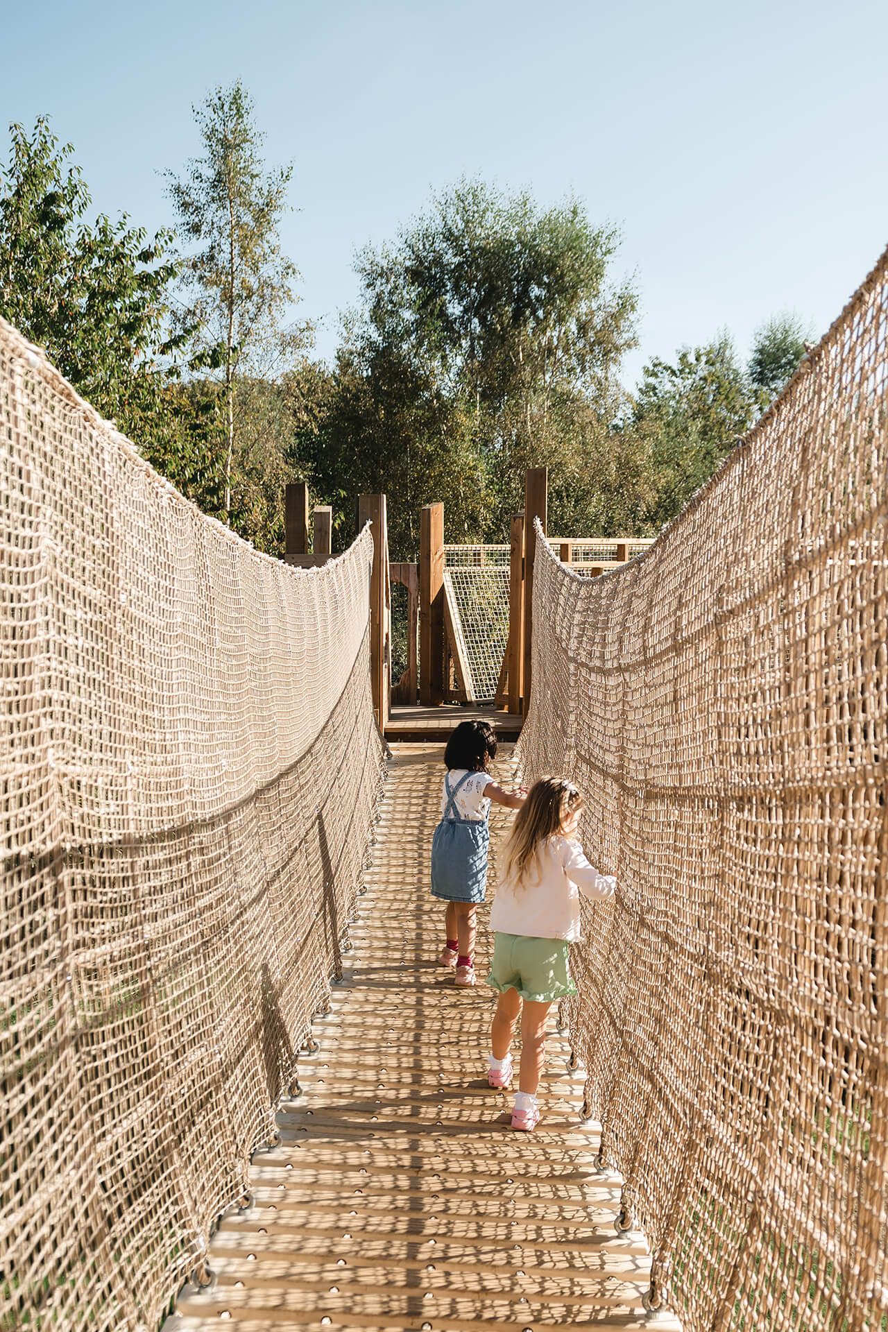 Two children walking across a rope bridge at the CAP.CO built adventure playground at Almond Valley photography by Lindsey Mack
