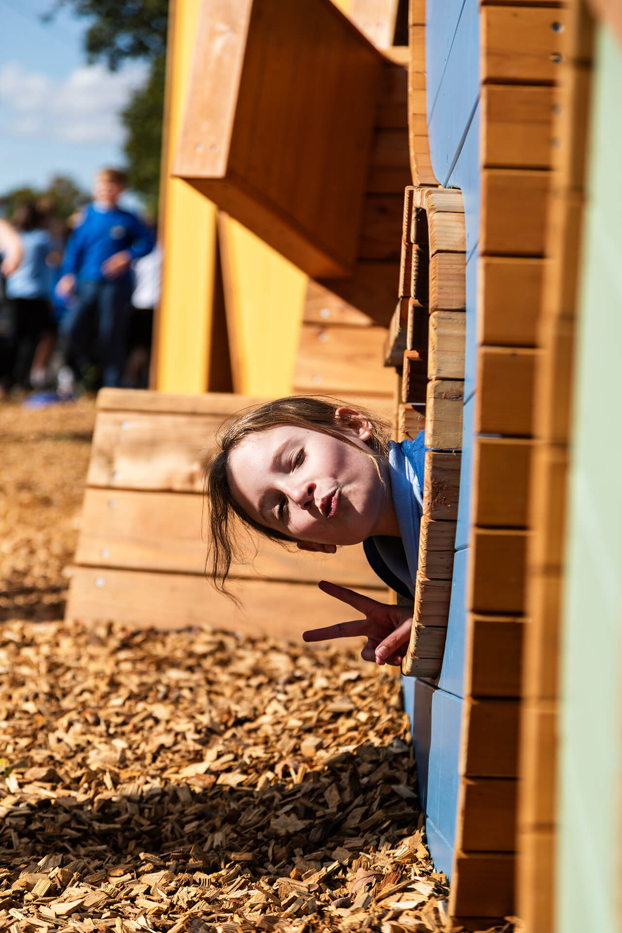 A girl poking her head out of the crawl space at Poringland school playground built by CAP.CO photography by Kev Foster