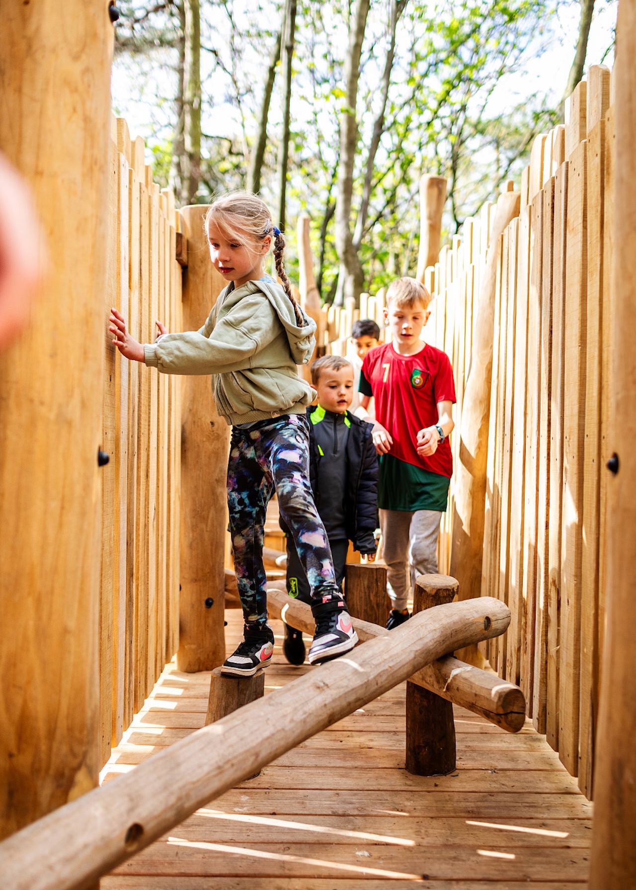 Kids eagerly navigating the balance beams on the walkway of the Woodland Adventures playground at The Belfry Hotel built and designed by CAP.CO photography by Kev Foster