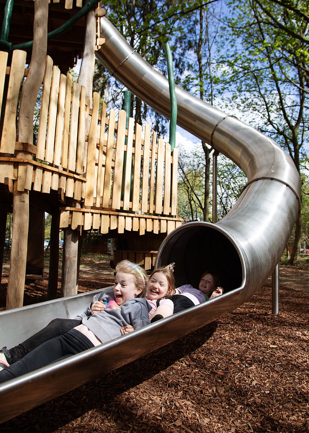 Three children having fun on the tube slide at the Woodland Adventures playground at The Belfry Hotel built and designed by CAP.CO photography by Kev Foster
