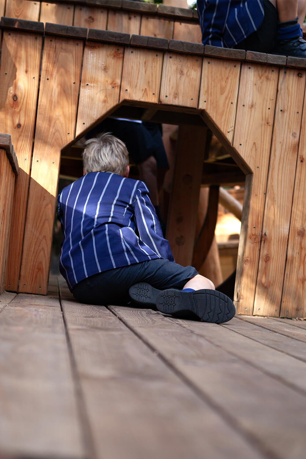 Child crawling through the timber hull of the wherry play structure at Town Close School, Norwich, designed and built by CAP.CO. Photography by George Browne