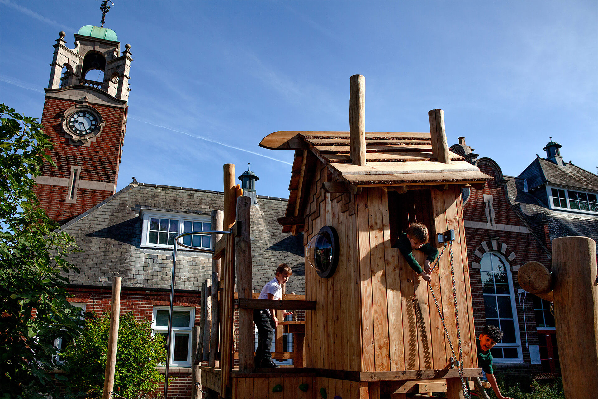 Child leaning out of the lookout window of the play tower with the Colman school clock tower behind, designed by CAP.CO. Photography by George Browne