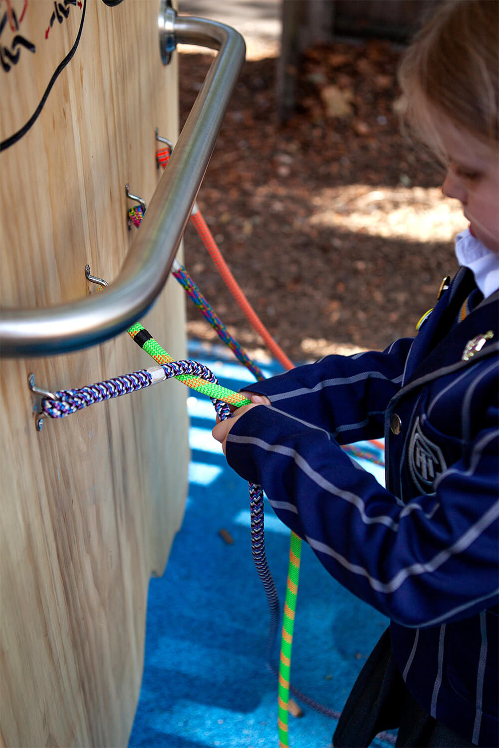 Child learning to tie knots on the “Know Your Knots” board with coloured ropes at Town Close School, by CAP.CO. Photography by George Browne