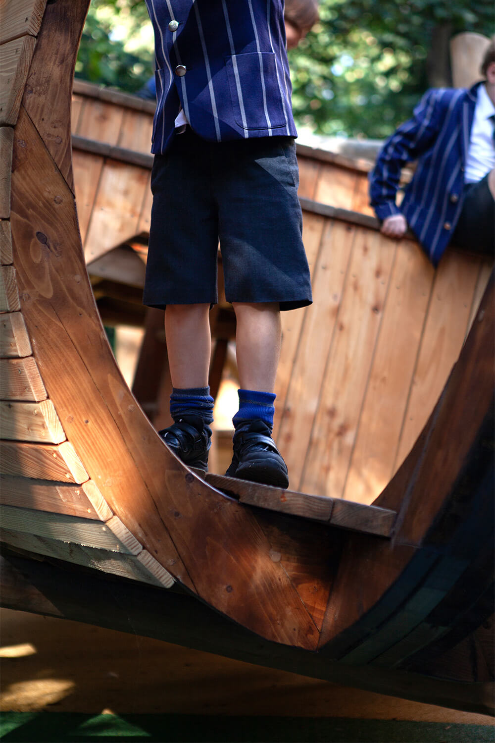Child standing in the curved timber hull of the wherry play structure at Town Close School, Norwich, designed and built by CAP.CO. Photography by George Browne