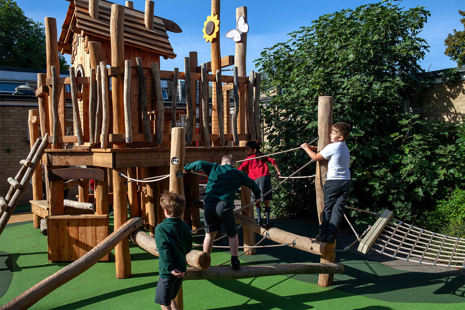Children balancing along logs and rope between robinia posts, with sunflower and butterfly details, at Colman Infant School by CAP.CO. Photography by George Browne