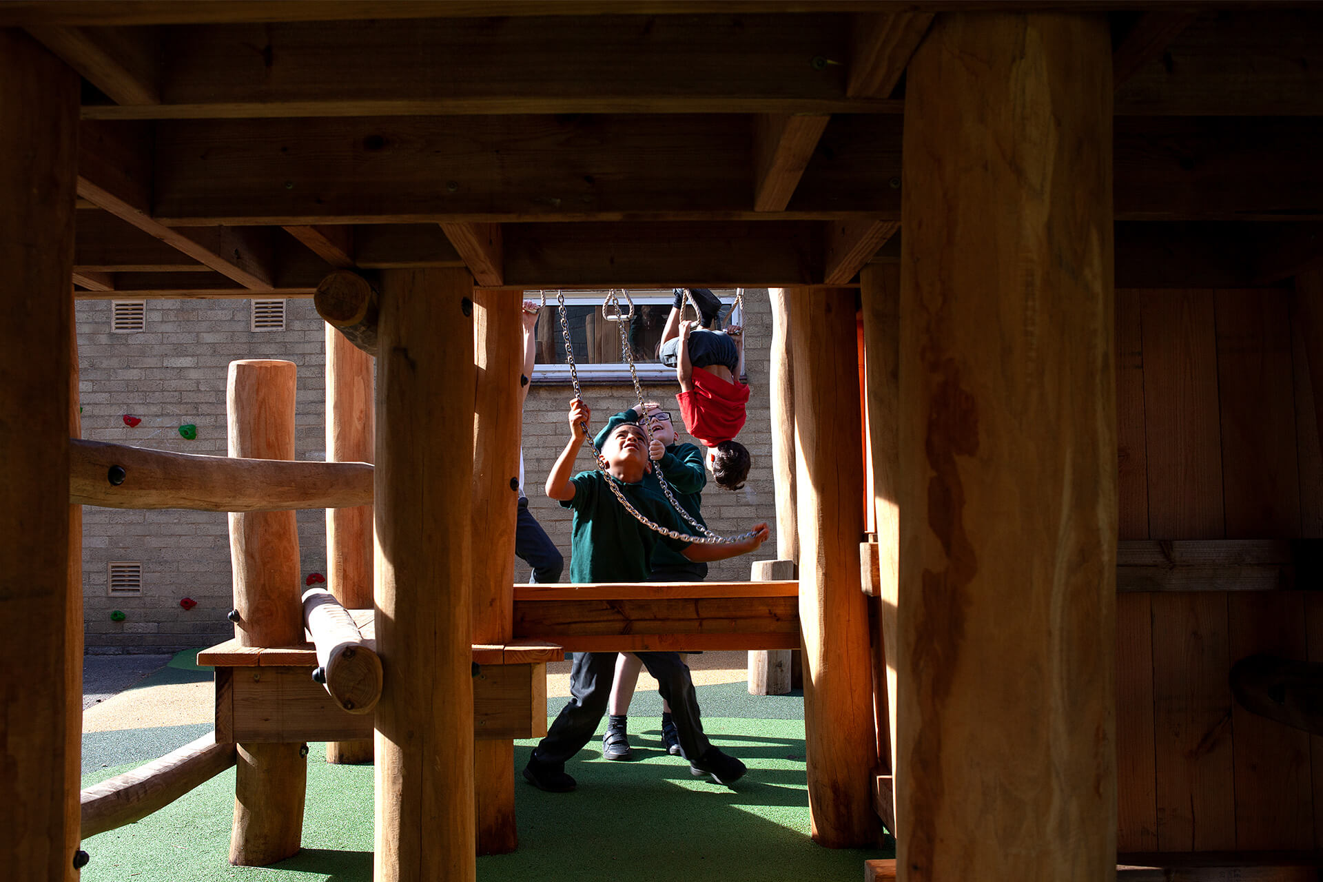 Children hanging from trapeze rings and chain handles beneath the play tower deck at Colman Infant School, by CAP.CO. Photography by George Browne