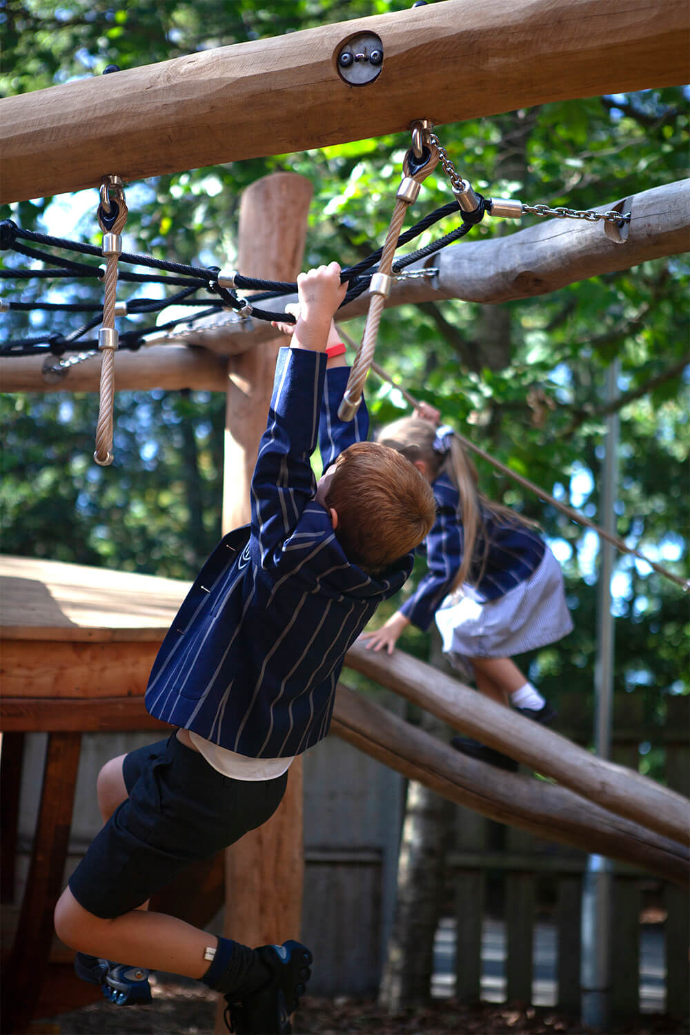 Children hanging from trapeze rings and climbing the log slope beside the wherry boat at Town Close School, designed by CAP.CO. Photography by George Browne