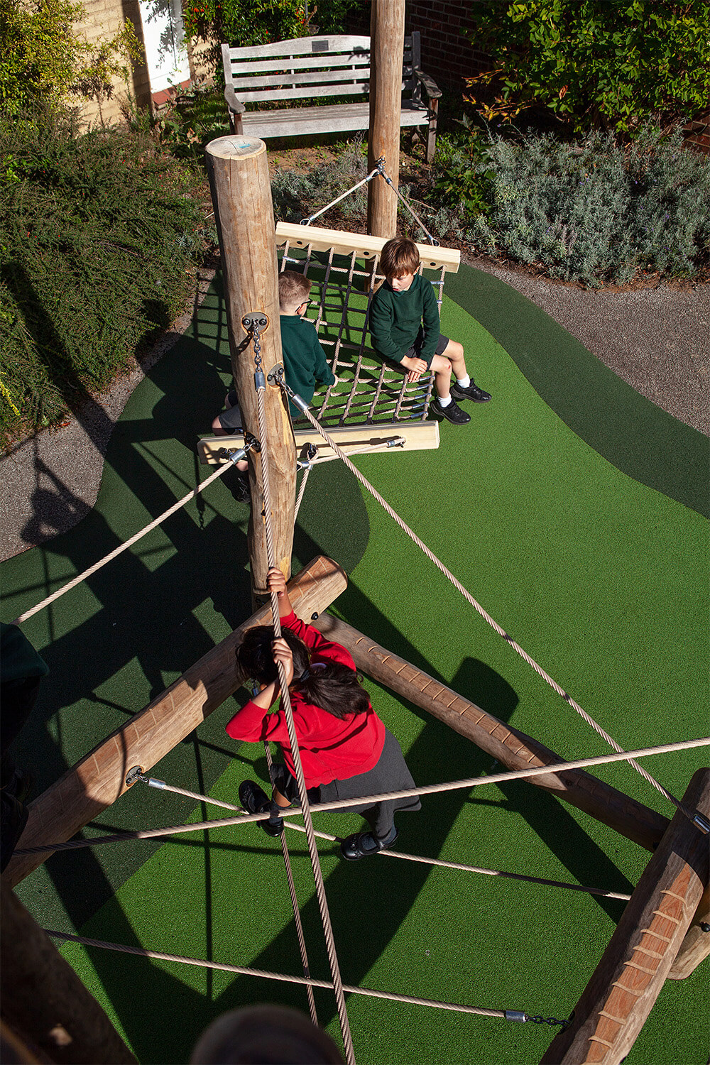 Children on the hammock swing seat and a girl climbing the rope net beside the play tower at Colman Infant School, Norwich, designed by CAP.CO. Photography by George Browne