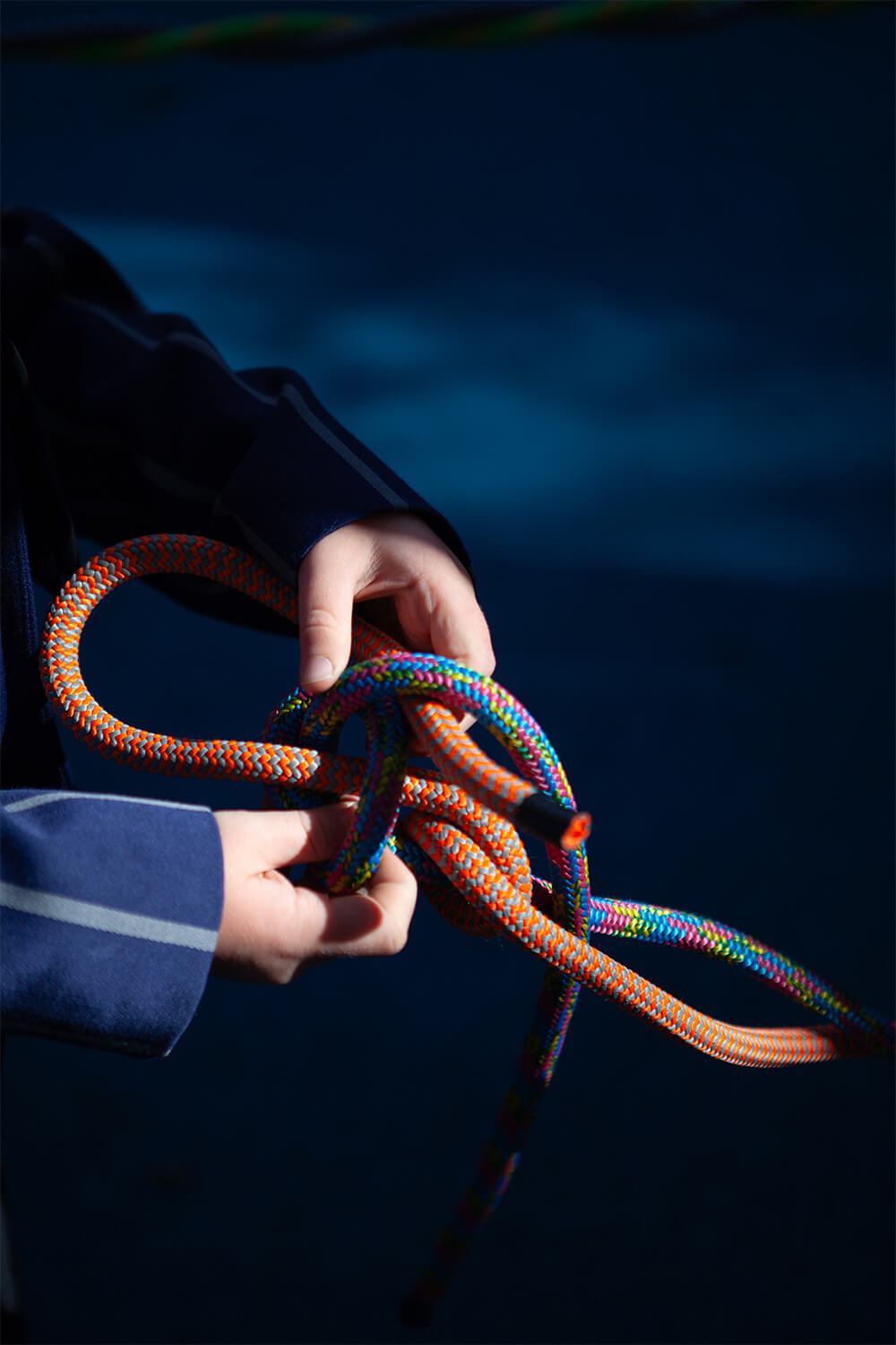 Close-up of a child’s hands tying a knot with bright orange and multicoloured rope at the Town Close School playground by CAP.CO. Photography by George Browne