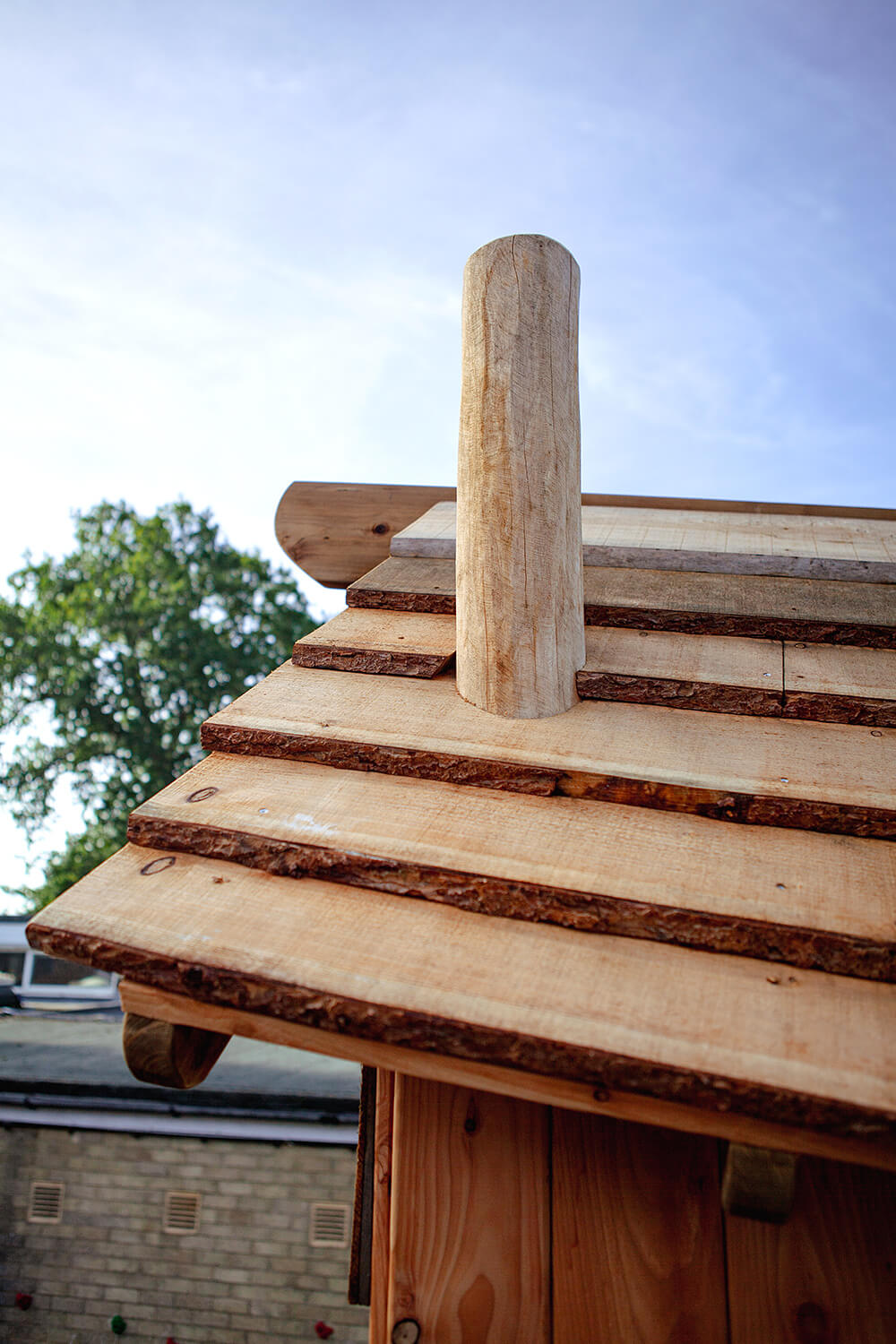 Close-up of the waney edge board roof and robinia post chimney on the play tower at Colman Infant School, designed by CAP.CO. Photography by George Browne