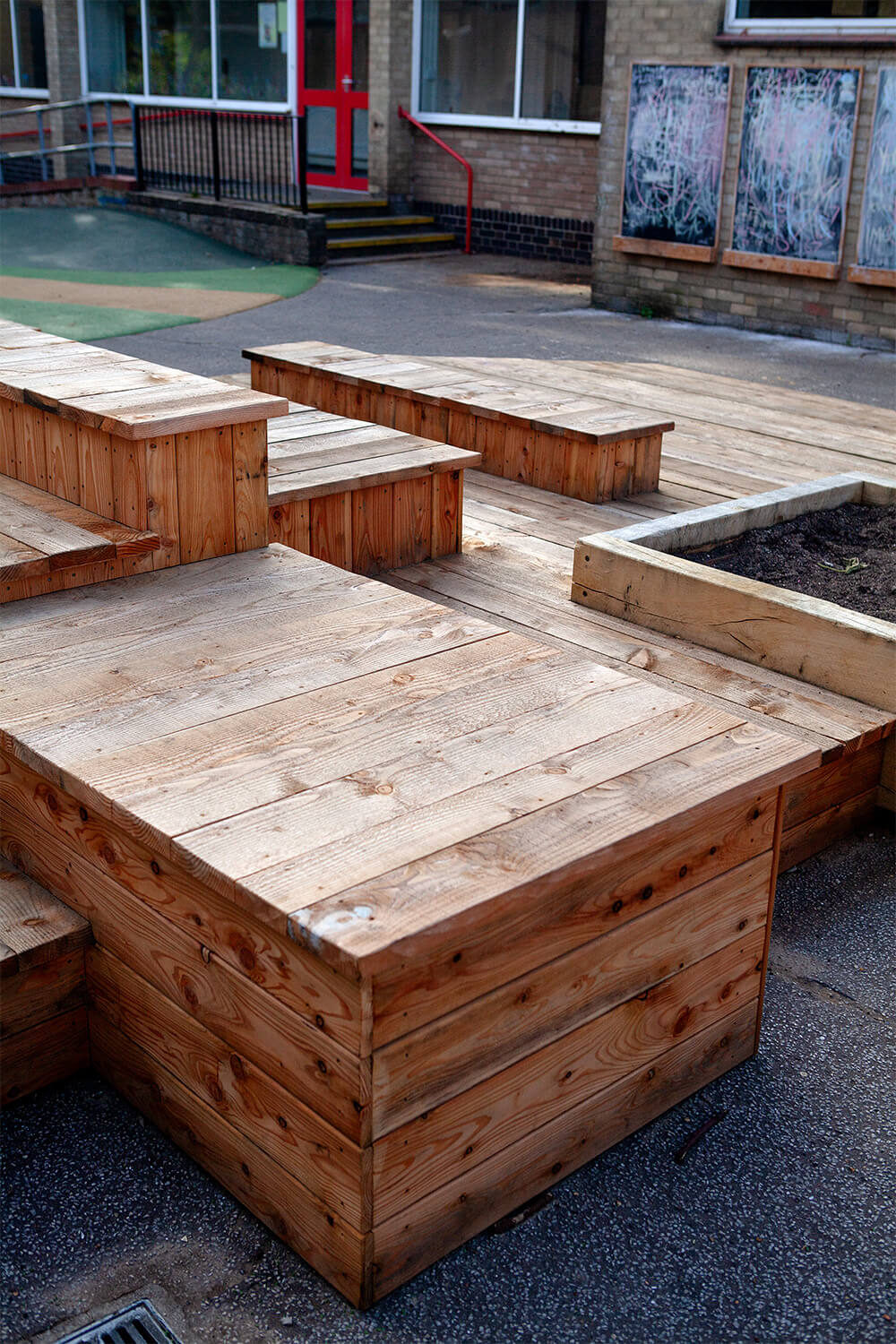 Stacked larch decks forming an outdoor classroom and performance space with chalkboards at Colman Infant School, built by CAP.CO. Photography by George Browne