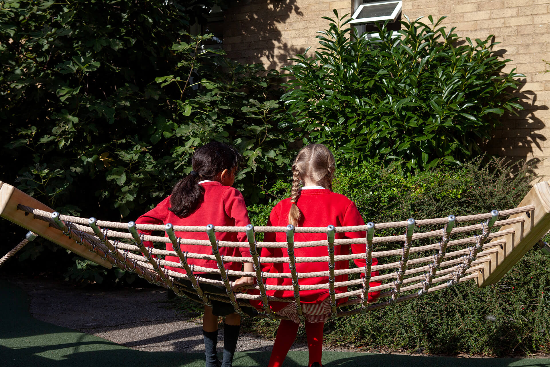 Two children sitting together on the rope hammock swing seat at Colman Infant School, designed by CAP.CO. Photography by George Browne